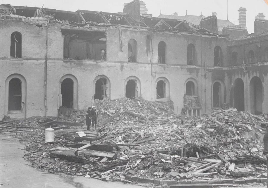 Grey and white photo showing the Royal Infirmary building damaged by war, with a pile of bricks and debris infront of the damaged walls.