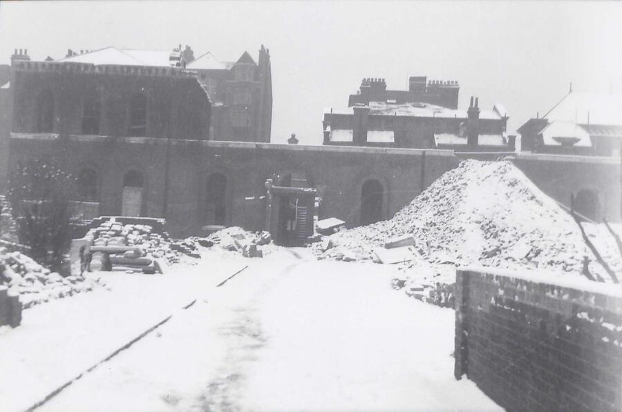 Black and white photo showing a building demolition. A huge pile of rubble and debris is piled high infront of the ruins of a brick building.