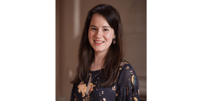 Alice Painting is facing the camera smiling. She has dark hair and is wearing a blue top with gold patterns.