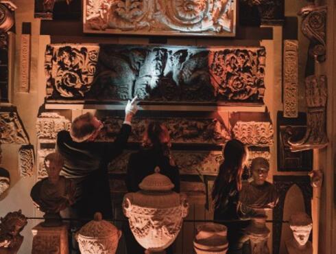 A man shines a torch on a sarcophagus while a young woman looks at it