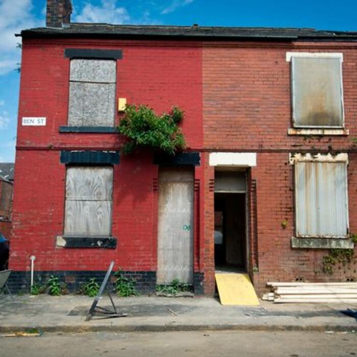 A street of boarded-up red brick terrace houses.
