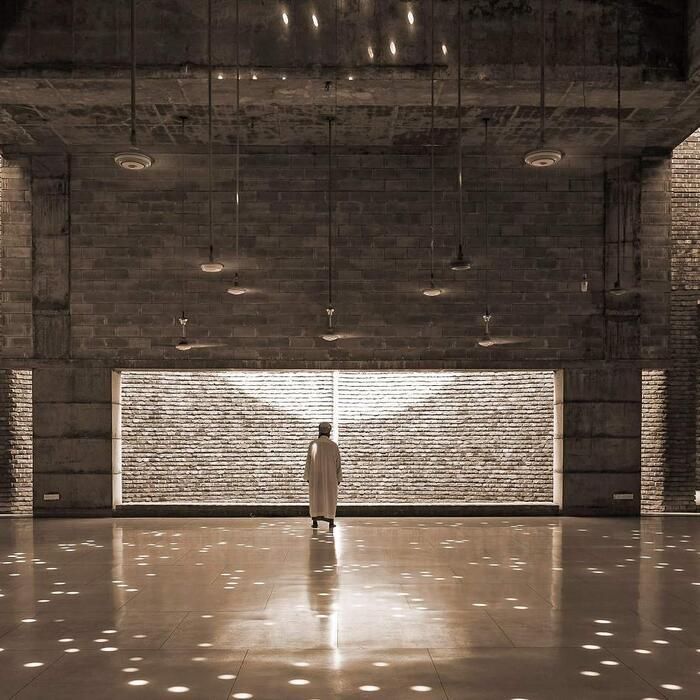 The interior of the Bait Ur Rouf Mosque, with spots and inlets of natural light illuminating a visitor in the vast main room.