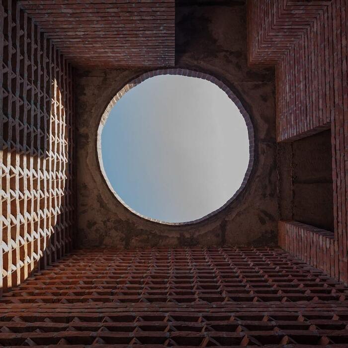 A circular skylight, build from patterns of red brick, letting sunlight into the space below.