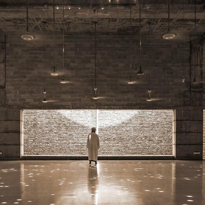 A photo of the inside of the Baitur Rauf Mosque, showing a lone visitor in a vast, beautifully lit space