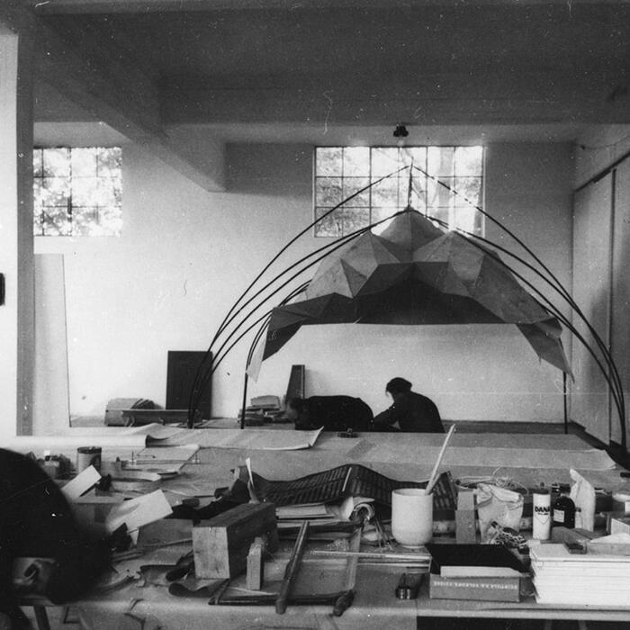 Black and white photo of office with large study model being worked on by an architect