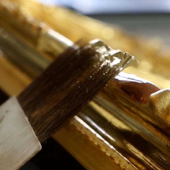 A brush applying gold leaf to the frame