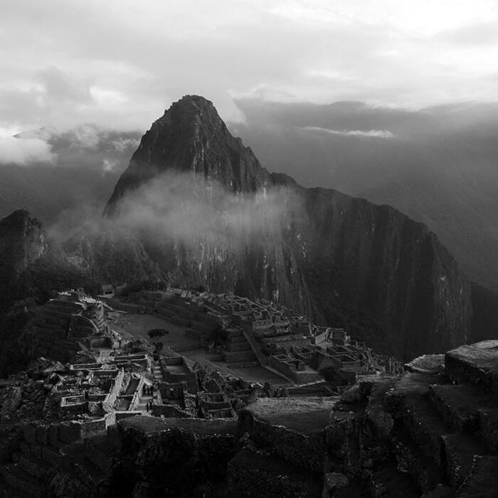 Machu Picchu, with sunlight shining onto the ruins, and clouds floating over the site