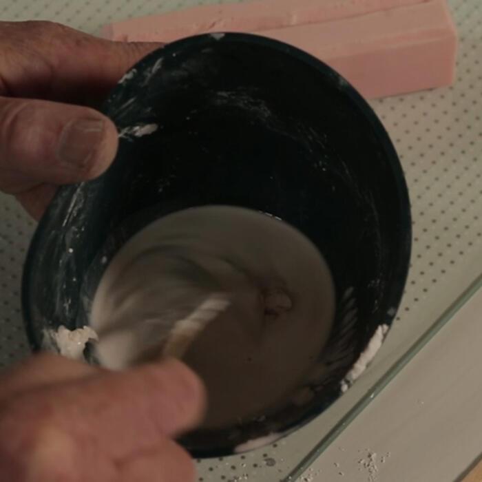 A conservator mixes plaster and water in a bowl