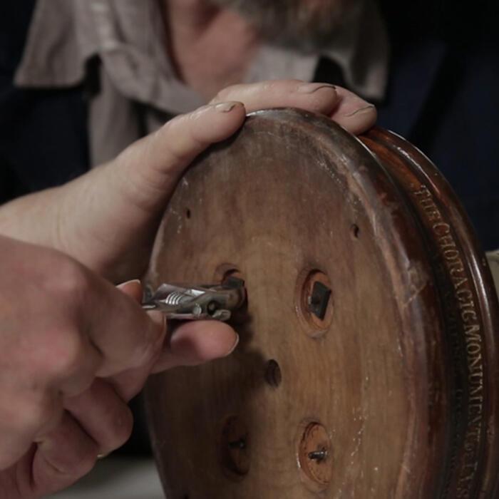 A conservator unscrewing the attachments on the base of the model with pliars