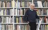 Kenneth Frampton, recipient of the 2019 Soane Medal, standing on a ladder in front of a row of bookshelves
