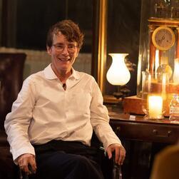 Architect Sophie Hicks, wearing a white shirt, sits in front of the Astronomical Clock in the Library-Dining Room.