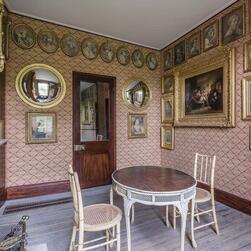 A small sitting room with a table and chairs, with many gold-framed mirrors and artworks on the walls.