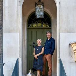 Two people standing in an arched doorway of a stone building with a green door and hanging lantern above.