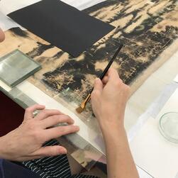 A conservator repairs the edging of the transparency by the application of new supporting strips.