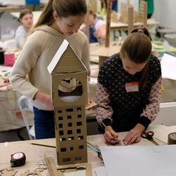 Two girls work together to craft a tower from cardboard and paper.