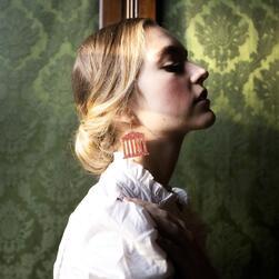 A woman again a green background wearing an earring shaped like a temple