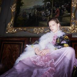 A woman in a purple dress in front of a Hogarth painting