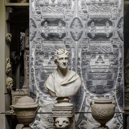 A grey patterned cloth in front of a marble bust of Sir John Soane