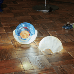 A glass sculpture depicting an eye, with the top lid separated on the floor. The glass eye is lit from behind making it illuminated.