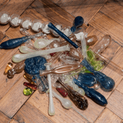 A pile of colourful glass lachrymatory (tear catchers) sculptures are piled on wooden floors.