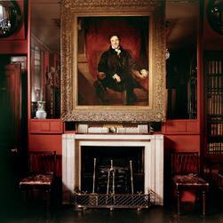 Portrait of Sir John Soane above his fireplace and a model of his design for the Houses of Parliament. A spotlight of natural light shines across his face.