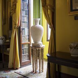 A white cermaic vessel on a golden stool is positioned in the window of the South Drawing Room.