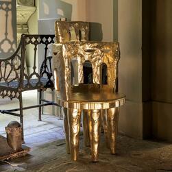 An eight-legged chair gilded with gold leaf, positioned in the Crypt of the Museum in relation to a nineteenth century garden chair.