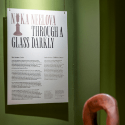 A white wall-text sits on a green wall, and reads 'Nika Neelova, Through a glass darkly' and explains in depth the curatorial inspiration and choices of the display.