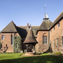 A view of Red House from the garden, showing a well with a conicle roof in the foreground.