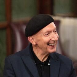 Stephen Jones, wearing a beret and a dark blue suit, laughing during the talk.