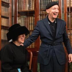 Stephen and Alice laughing. Alice is earing a low-sitting black hat that obscures her vision.