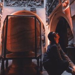 A man kneels down on the floor, looking upwards, sorting out red uplighters in the basement of Sir John Soane's Museum. Behind him is the Sarcophagus of Seti I.