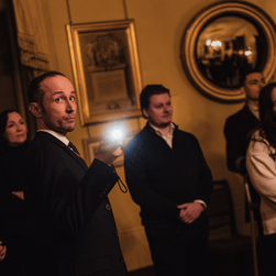 A VA talking to a tour group and pointing a torch at the Owens portrait of Sir John Soane in the South Drawing Room .