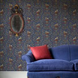 terior scene with a deep blue upholstered sofa and a red cushion in front of a wall covered in dark blue wallpaper featuring a repeating pattern of stylized animals and floral motifs in gold and red. An ornate oval mirror with a decorative frame hangs on the wall, and a patterned rug is visible on the floor